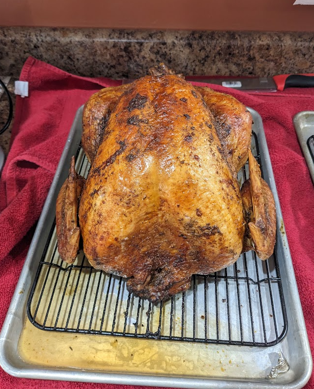 Back side of a finished smoked turkey resting on a rack