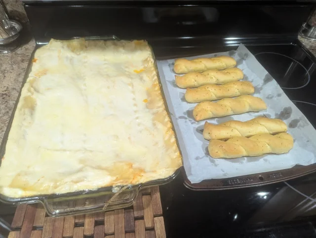 Finished Two-Sauce Lasagna in a glass dish beside breadsticks
