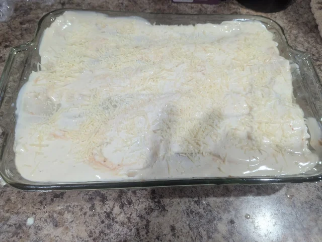 Unbaked Two-Sauce Lasagna topped with Alfredo sauce and Parmesan in a glass dish